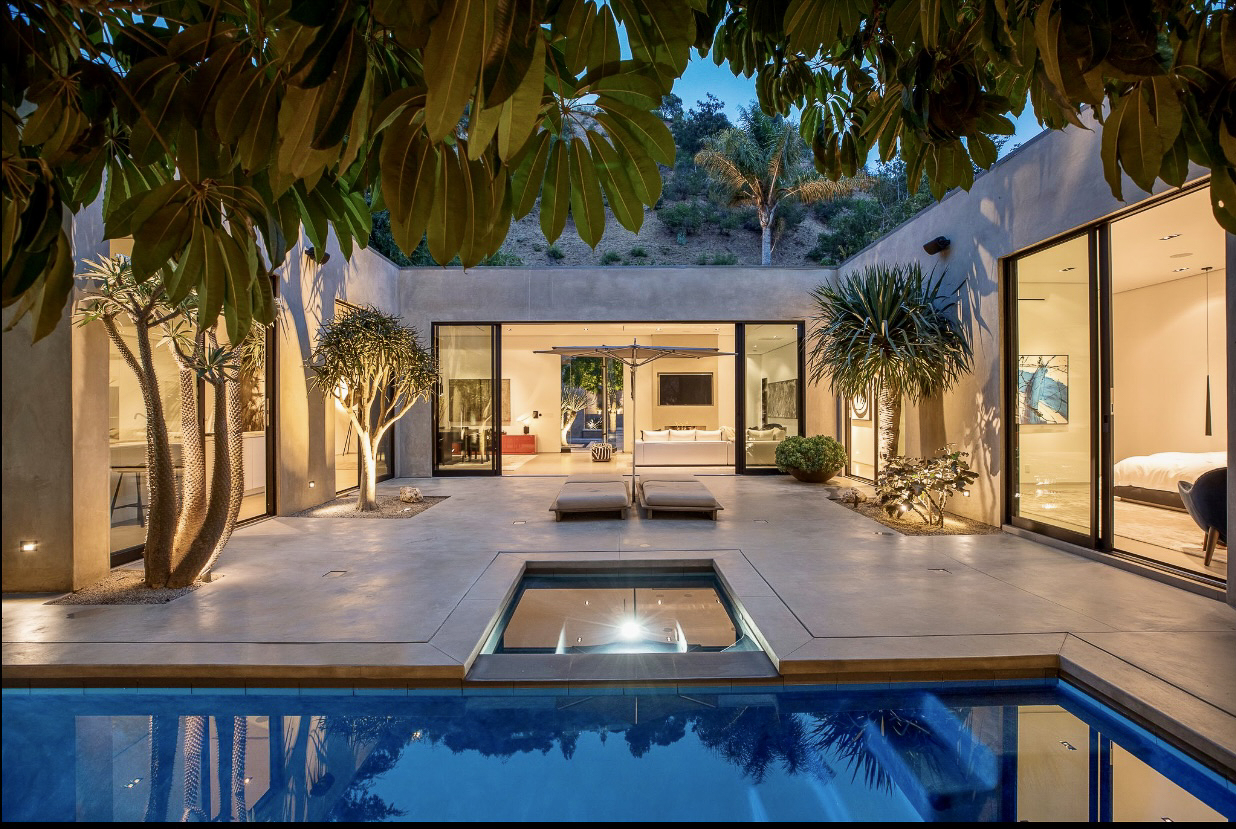 Modern house with pool at twilight, spacious patio, and open living area visible through glass doors.