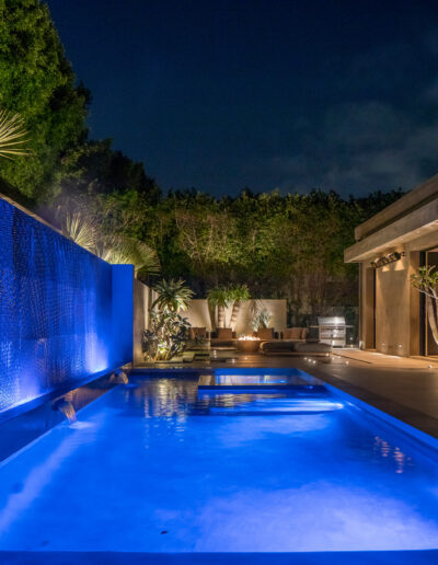 Illuminated swimming pool and patio area at night with architectural lighting and landscaping.