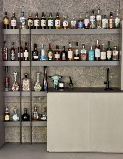 A neatly organized bar with a selection of spirits on shelves above a closed cabinet.